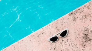 Chic white sunglasses resting on a pink poolside next to clear blue water, perfect for summer vibes.
